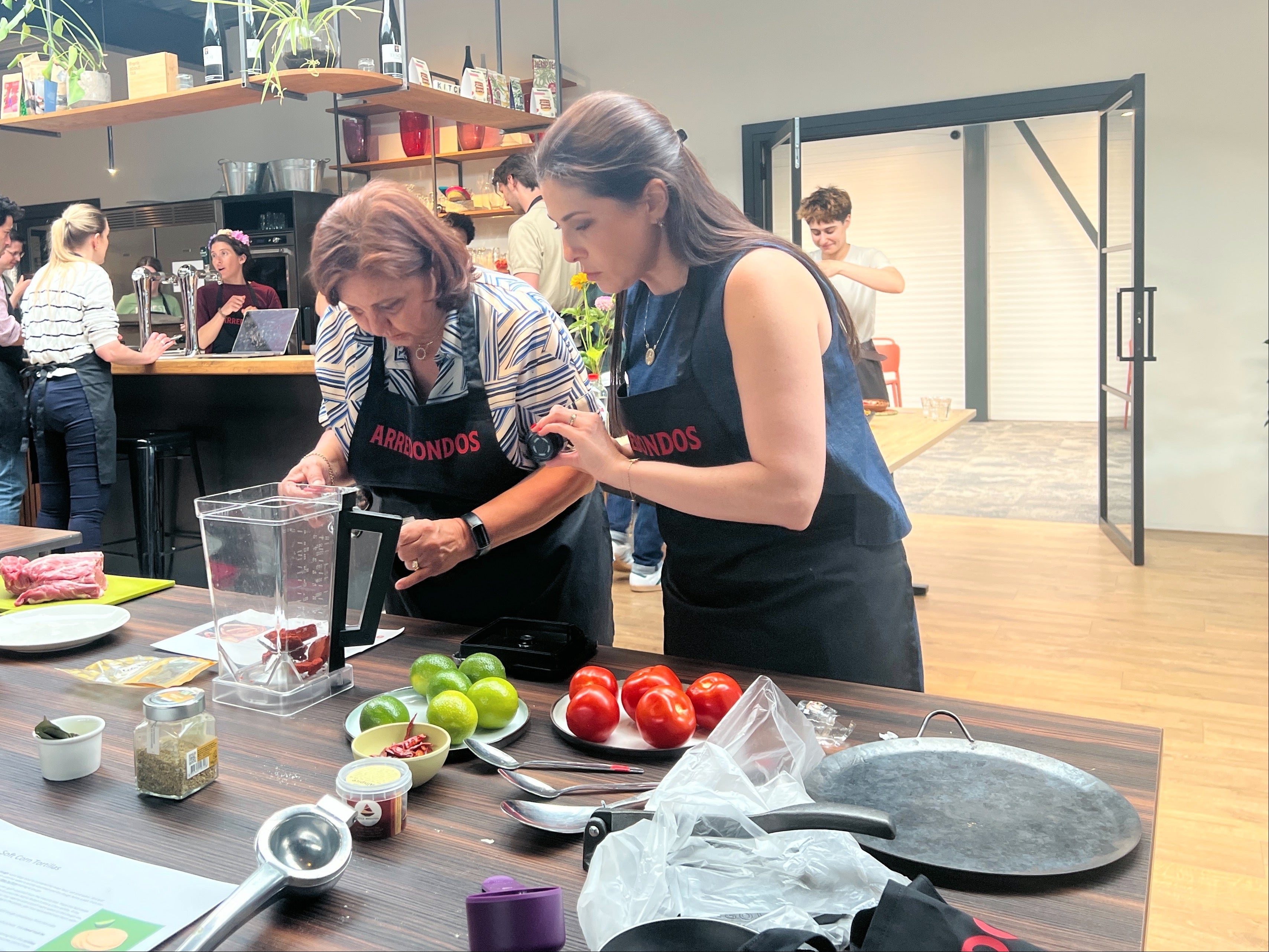 Two women in a kitchen setting, one using a food processor with ingredients on the counter.